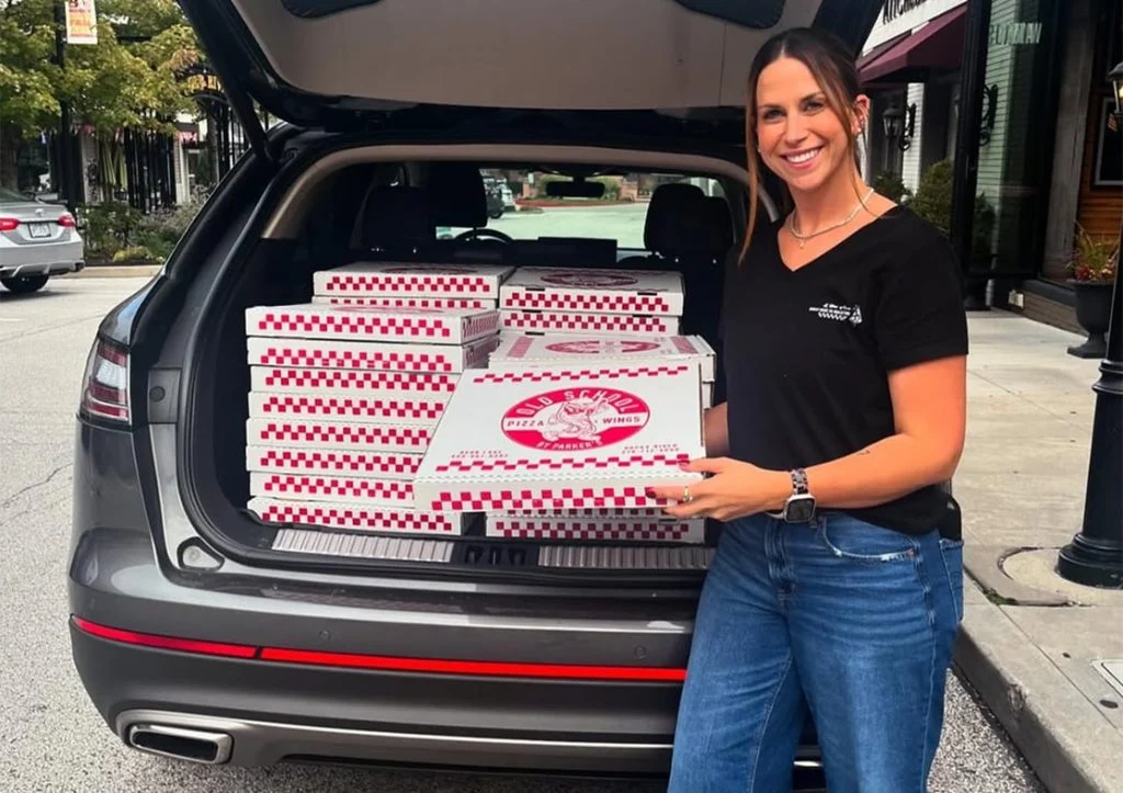 woman holding old school pizza box with multiple in her trunk